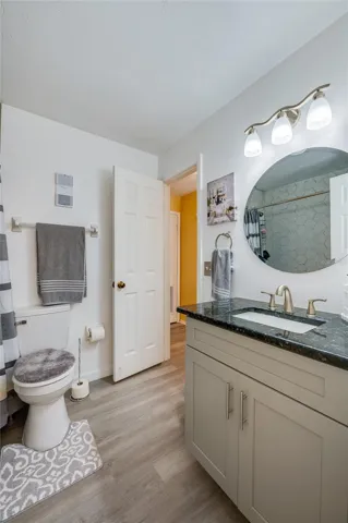 Full bathroom featuring a vanity with dark granite countertops, LVP flooring, and a circular wall mirror.