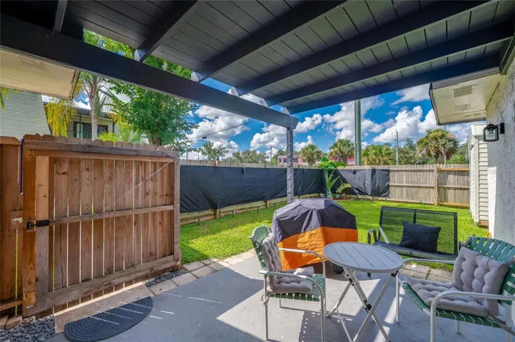 Covered ground-floor patio leading out to a fully fenced private yard framed by lush green grass.
