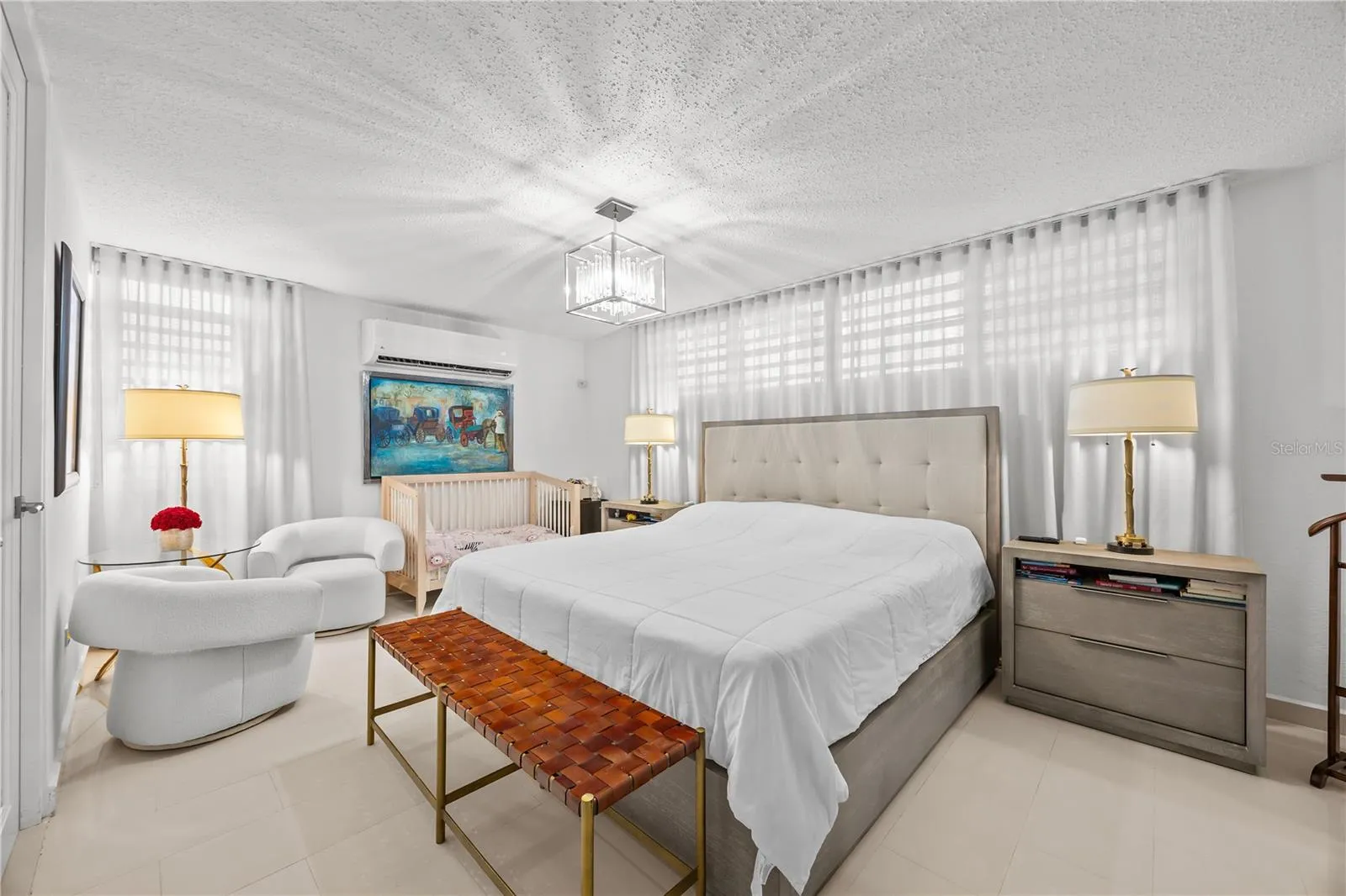 Spacious primary bedroom with room to relax, featuring a sitting nook, air conditioning, and soft natural light through sheer drapery