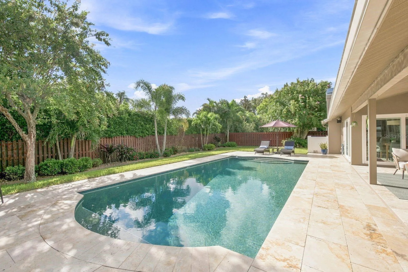 Sleek pebble tech pool with travertine pavers