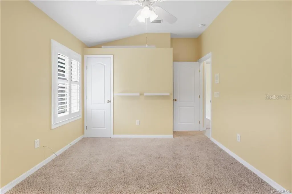 BEDROOM 2 – Alternate view showing the lighted plant shelf, plantation shutters, closet &amp; additional wall shelving.