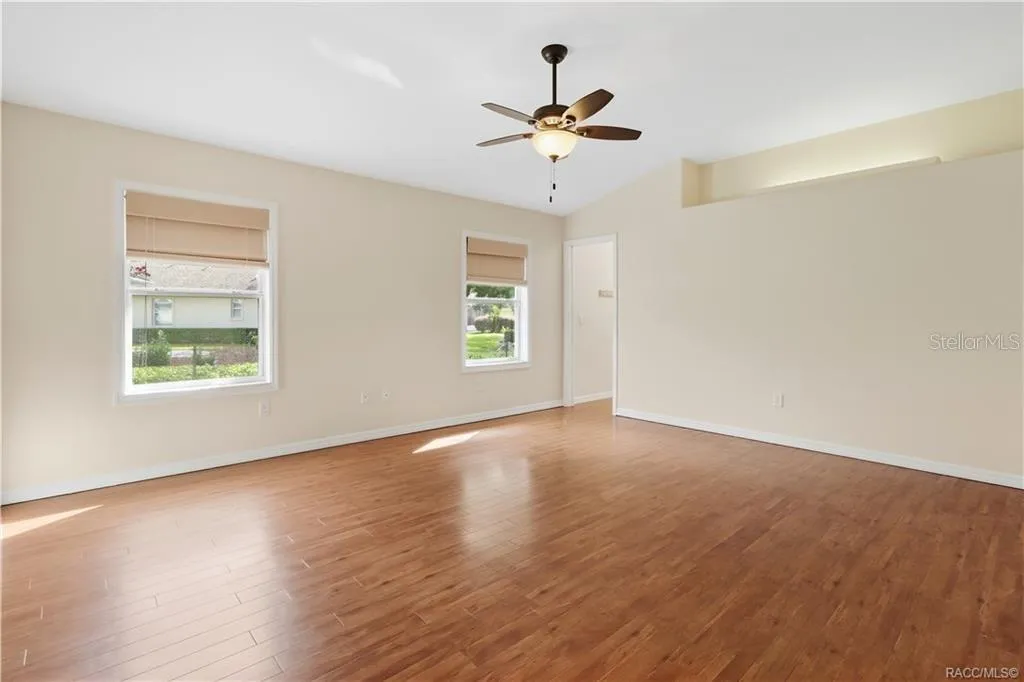 PRIMARY BEDROOM – Spacious primary bedroom featuring LUXURY VINYL PLANK FLOORING, ceiling fan, lighted plant shelf, neutral walls &amp; two windows providing natural light.