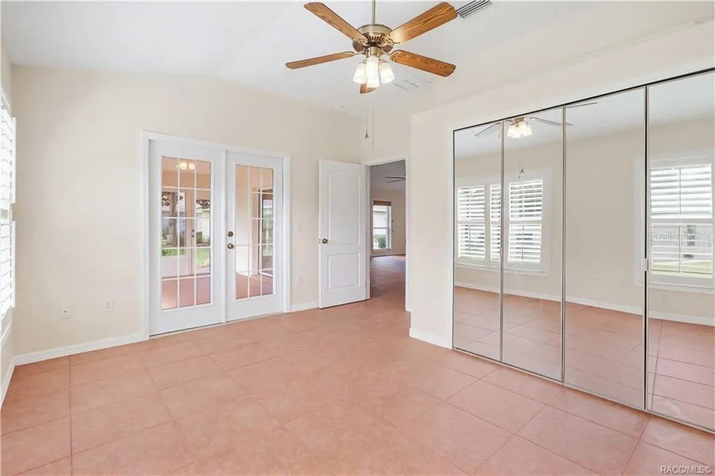 FLEX ROOM / DEN / 4th BEDROOM – Alternate view highlighting mirrored closet doors, French doors entering enclosed Florida room, tile flooring, ceiling fan &amp; plantation shutters.