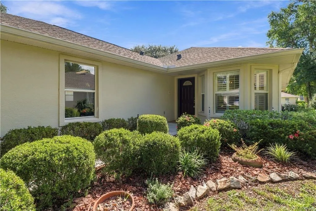 COVERED ENTRY – A closer look at the sheltered front entrance surrounded by mature landscaping. The grouping of front windows with plantation shutters gives the home a polished appearance from both inside &amp; out.