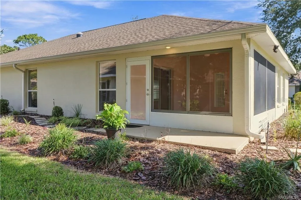 REAR EXTERIOR / SUNROOM – Exterior view of the enclosed sunroom with screened/windowed walls, exterior access &amp; surrounding landscaped beds.