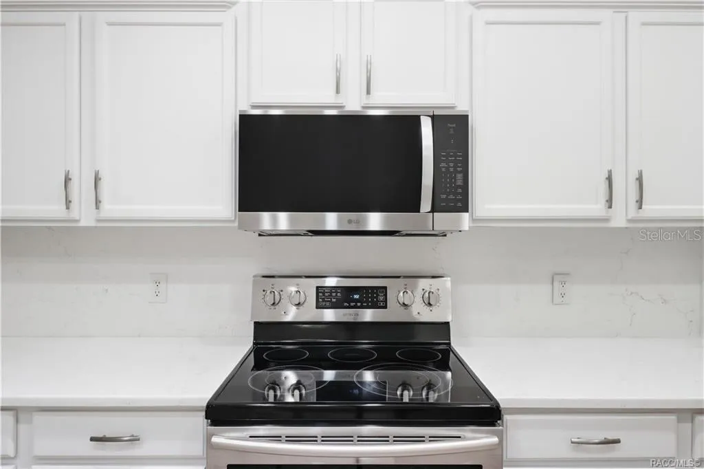 APPLIANCE DETAIL – Close-up of the stainless-steel electric range and microwave hood surrounded by crisp white cabinetry, quartz countertops &amp; coordinating backsplash for a fresh, modern presentation.