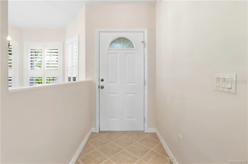FOYER – Bright entry foyer with neutral tile flooring laid on the diagonal, crisp white trim &amp; a front door featuring a decorative half-moon glass insert. Plantation shutters on the adjacent windows add both style &amp; light control.