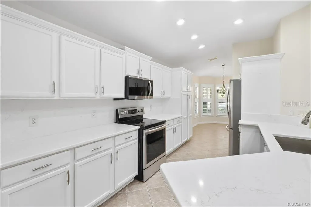 KITCHEN – Clean, bright finishes define the remodeled kitchen with white raised-panel cabinetry, modern hardware, quartz countertops &amp; backsplash, stainless-steel range and built-in microwave. Recessed lighting keeps the workspace bright.