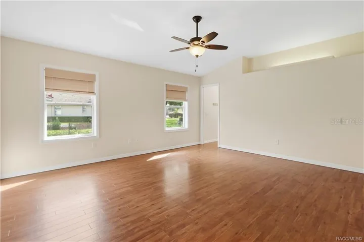 PRIMARY BEDROOM – Spacious primary bedroom featuring LUXURY VINYL PLANK FLOORING, ceiling fan, lighted plant shelf, neutral walls &amp; two windows providing natural light.