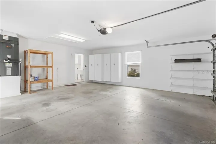 2-CAR GARAGE / STORAGE – Alternate garage view showcasing additional storage with wall-mounted cabinets, wire shelving, freestanding shelving &amp; access to the interior laundry room.