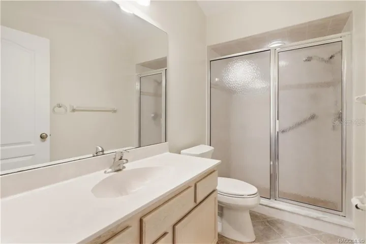 GUEST BATHROOM – Full guest bath with vanity, large wall mirror, tile flooring &amp; shower with textured glass enclosure.