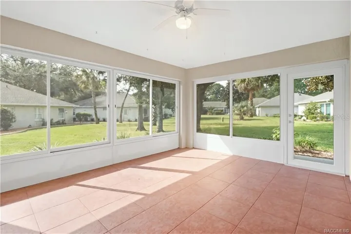 ENCLOSED SUNROOM – Expansive enclosed sunroom surrounded by large windows overlooking the landscaped backyard, with tile flooring, ceiling fan &amp; exterior door.