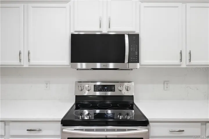 APPLIANCE DETAIL – Close-up of the stainless-steel electric range and microwave hood surrounded by crisp white cabinetry, quartz countertops &amp; coordinating backsplash for a fresh, modern presentation.
