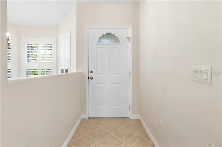 FOYER – Bright entry foyer with neutral tile flooring laid on the diagonal, crisp white trim &amp; a front door featuring a decorative half-moon glass insert. Plantation shutters on the adjacent windows add both style &amp; light control.
