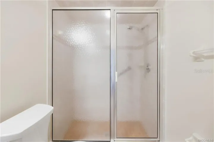 GUEST BATHROOM – SHOWER – Closer view of the shower with textured sliding-glass enclosure &amp; tiled surround.
