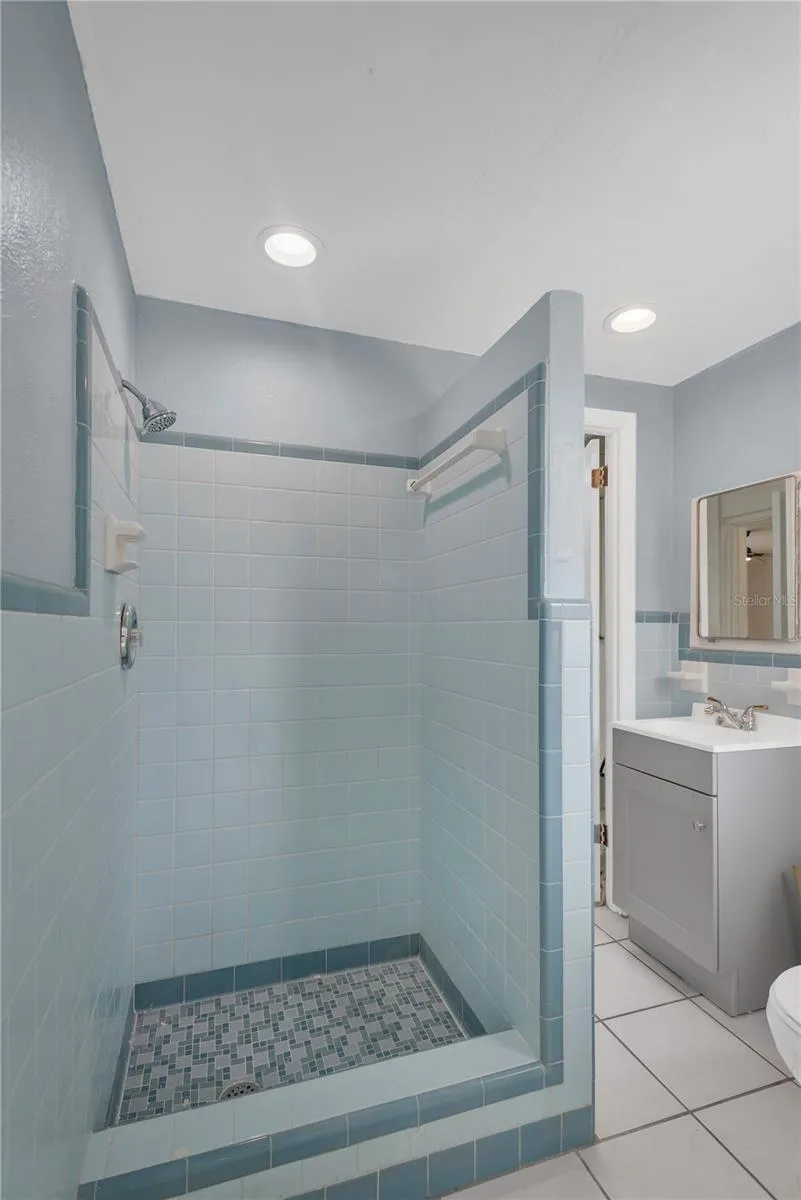 The spacious shower stall showcases the timeless charm of the original tile, beautifully preserved to highlight its nostalgic character and enduring appeal.