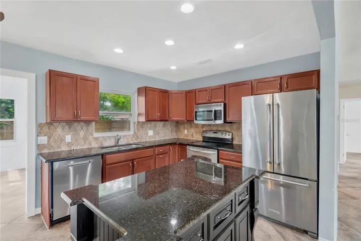 Remodeled kitchen is designed for both everyday living and entertaining, with a central island workspace, wood cabinetry, granite countertops, and sleek stainless-steel appliances.