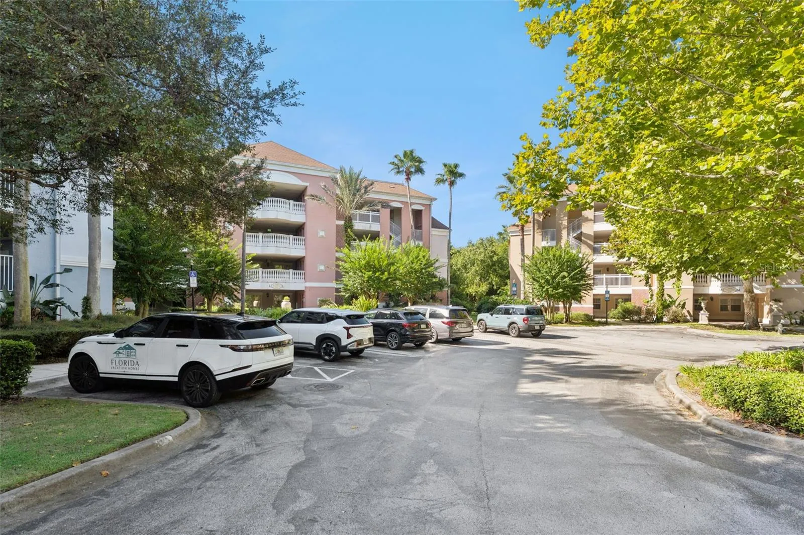 Community Parking: Ample surface parking area in front of the condo buildings, framed by mature trees and lush greenery.