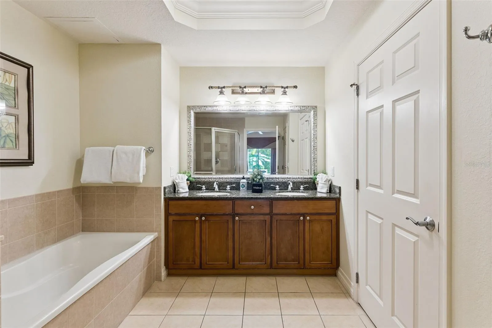 Primary Bathroom Double Vanity: Primary suite vanity featuring dual undermount sinks, rich wood cabinetry, granite counters, decorative framed mirror, and an updated vanity light bar.
