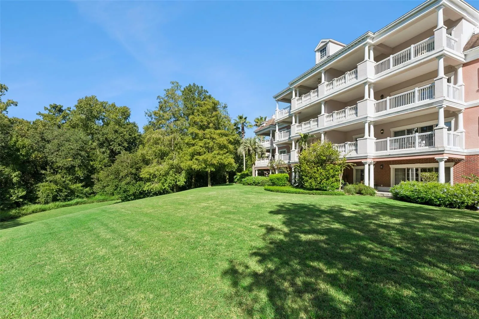 Building &amp; Grounds View: Angled exterior view highlighting the sprawling lawn, shaded tree line, and private balconies of the condo community.