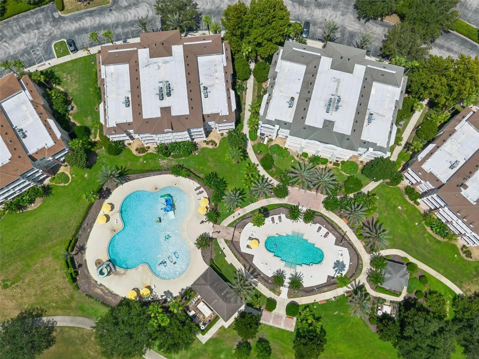Overhead View of Pool Complex: Direct top-down drone capture showcasing the dual resort pools, splash play area, sunbathing decks, and surrounding condo buildings.