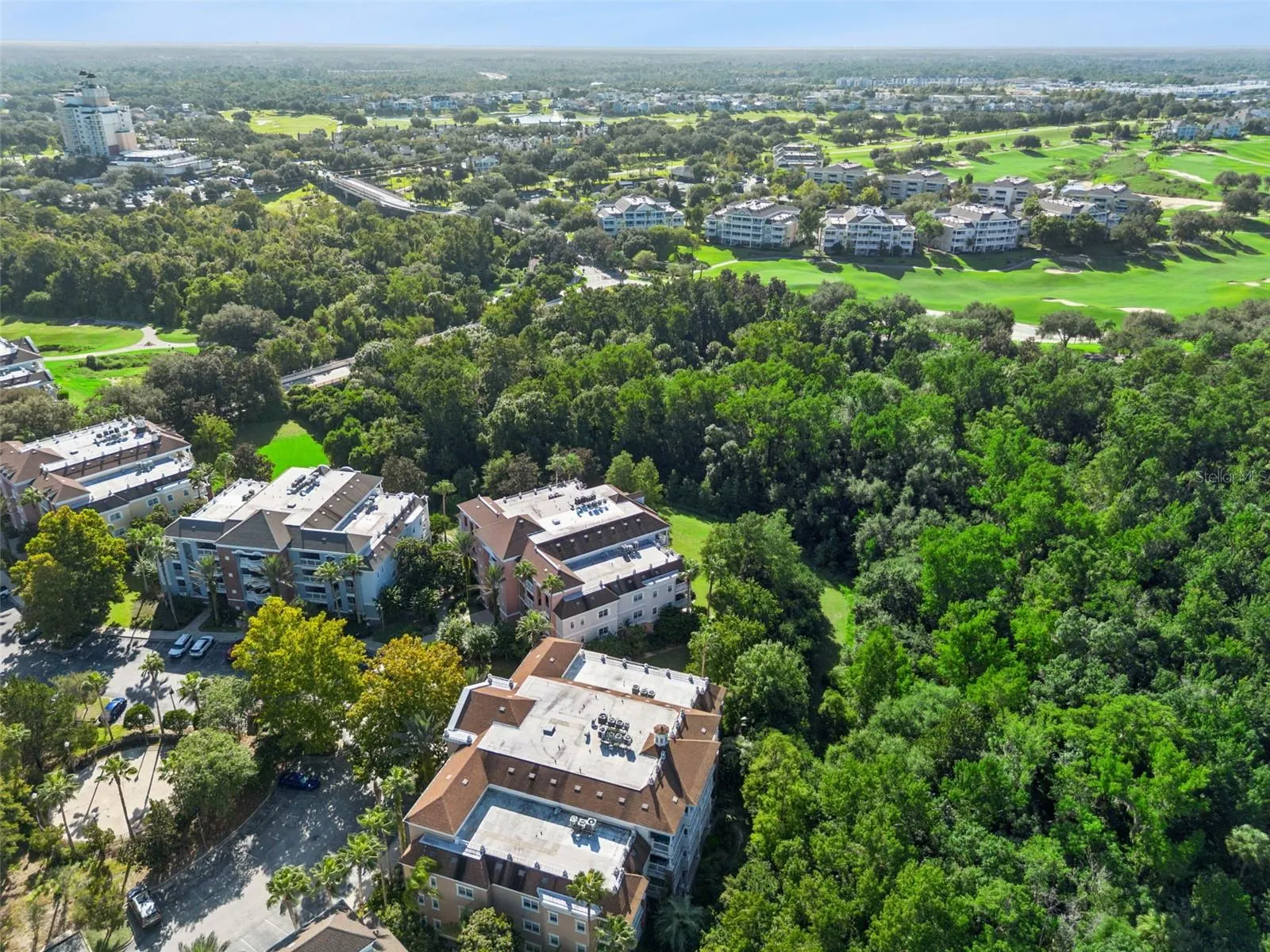 Aerial View of Complex: High-angle aerial capture showing the condo complex tucked into lush forest foliage adjacent to golf course fairways.