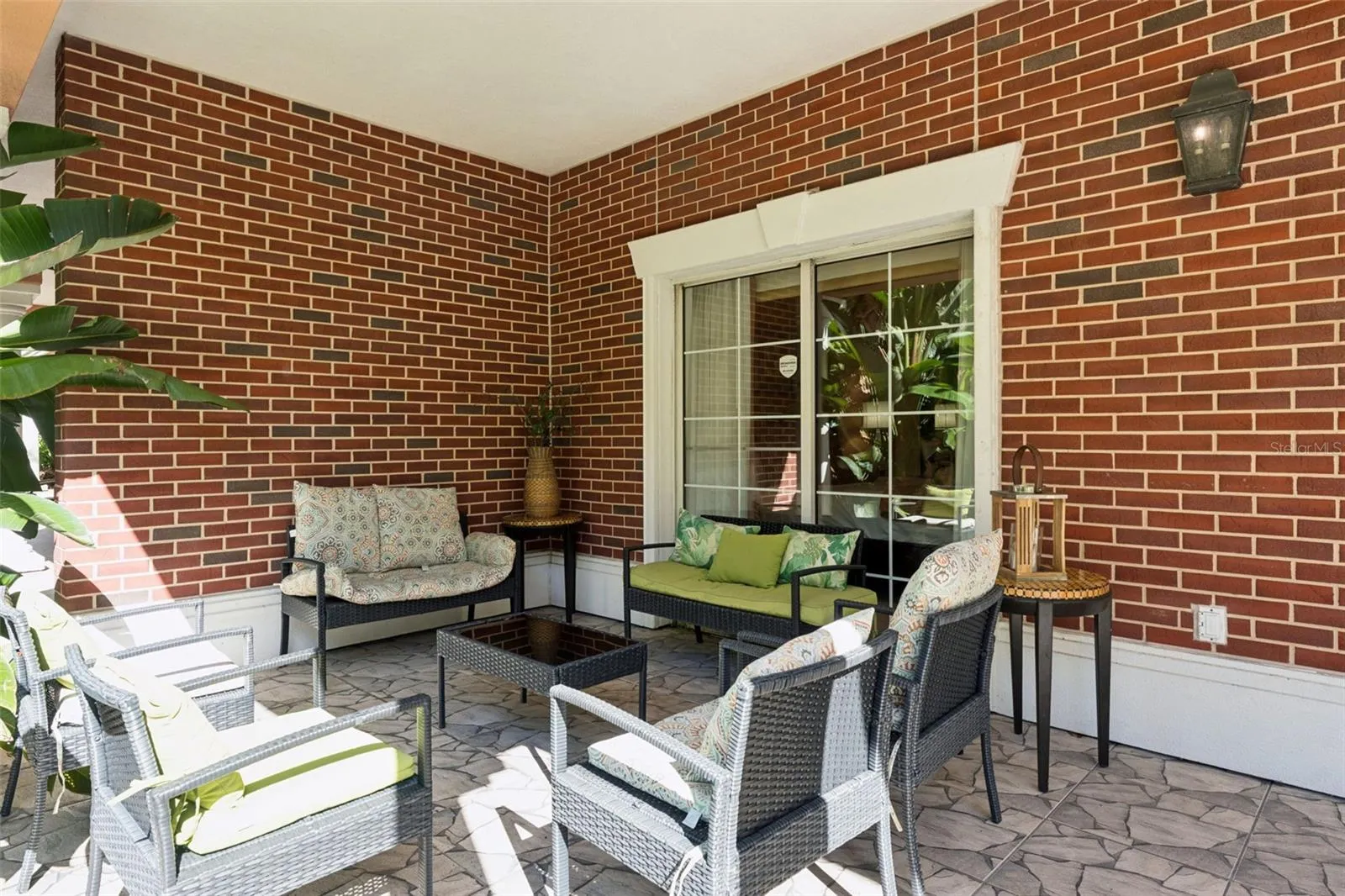 Covered Outdoor Patio: Expansive covered outdoor patio featuring classic red brick accent walls, stone-patterned tile flooring, sliding door access, and ample space for lounge seating.