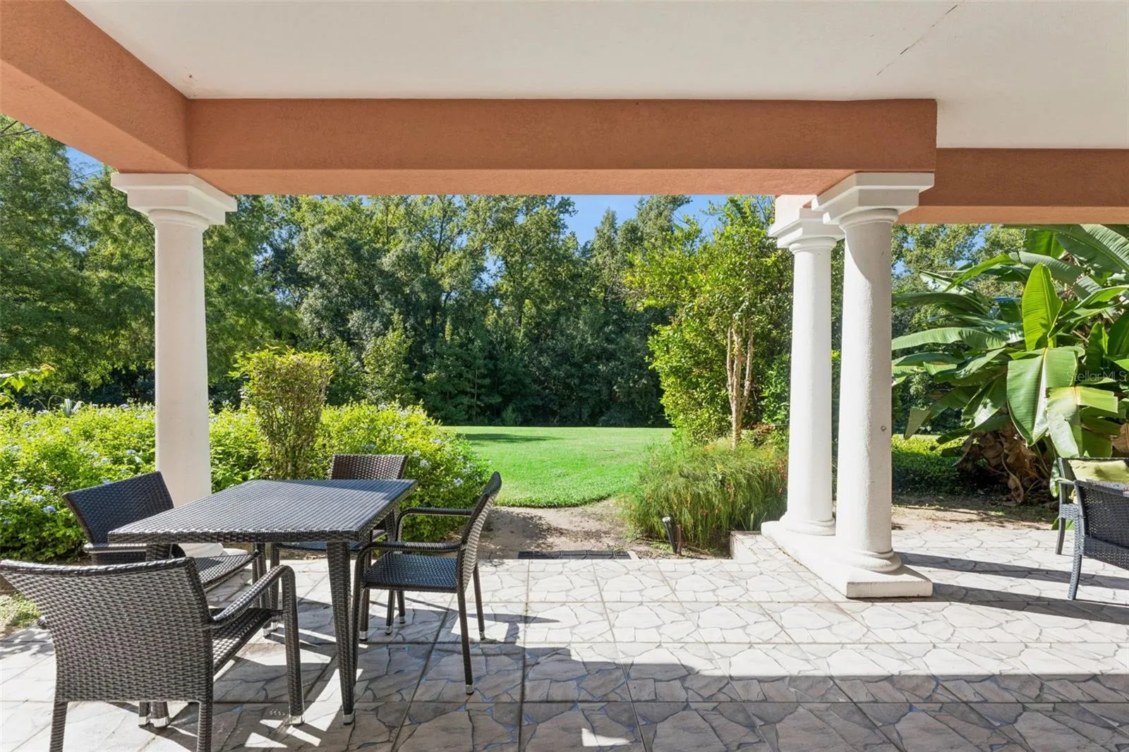 Covered Porch Lawn View: Direct view from the covered patio framed by architectural columns looking out onto an expansive green lawn and dense private tree line.