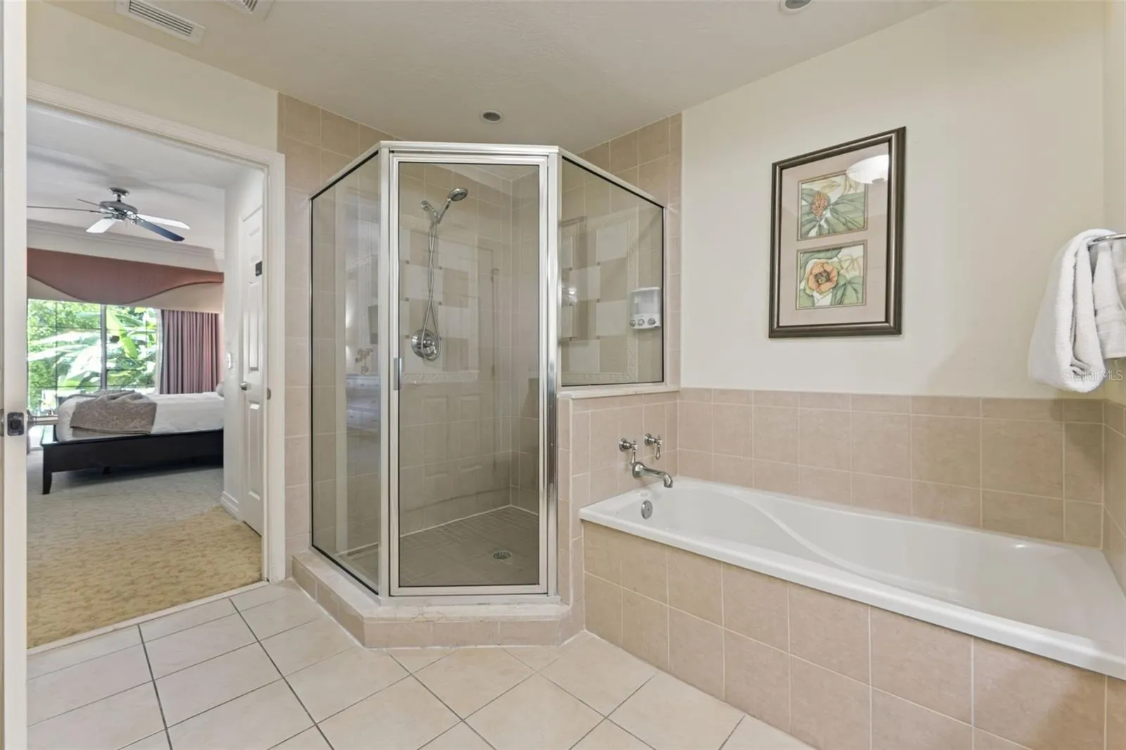 Primary Bathroom &amp; Soaking Tub: Ensuite primary bath equipped with a glass-framed corner walk-in shower, separate soaking tub with neutral tile surround, and tile flooring.