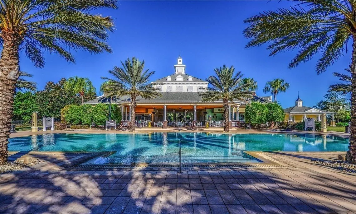 Resort Pool &amp; Community Clubhouse: Sun-drenched resort swimming pool framed by tall palm trees, showcasing the grand community clubhouse and covered patio pavilion.