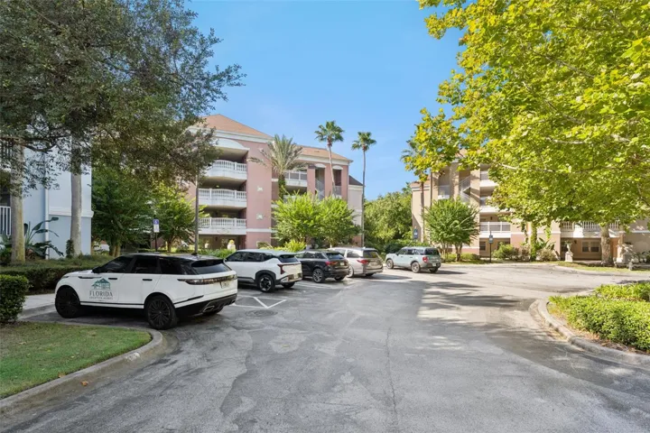 Community Parking: Ample surface parking area in front of the condo buildings, framed by mature trees and lush greenery.
