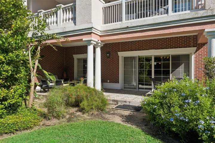 Ground-Floor Exterior &amp; Patio: Ground-floor exterior view showcasing the unit's private covered patio, brick accents, sliding glass entry, and surrounding flower beds.