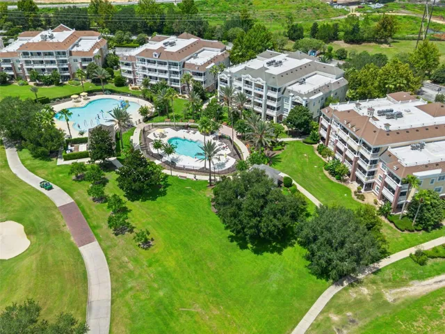Pool Amenities &amp; Fairway View: Elevated aerial shot highlighting the resort pool grounds, paved golf cart paths, expansive green lawns, and residential buildings.