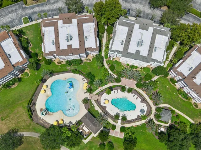 Overhead View of Pool Complex: Direct top-down drone capture showcasing the dual resort pools, splash play area, sunbathing decks, and surrounding condo buildings.