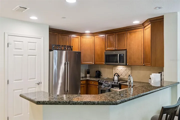 Kitchen Wrap-Around Bar: Angle highlighting the generous wrap-around granite counter space, deep wood upper and lower cabinetry, tile floor, and stainless steel appliances.