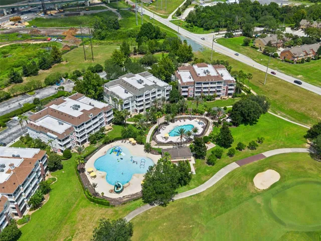 Resort Community Aerial: High-angle aerial view displaying the resort pool complex, multi-story condo buildings, resident parking, and adjoining golf course fairway.