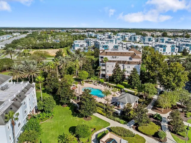 Neighborhood Pool &amp; Grounds Aerial: High-angle aerial view of the neighborhood pool, paved walking trails, lush green spaces, and surrounding multi-story condo buildings.