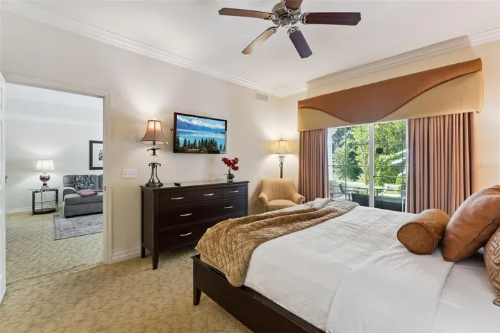 Primary Suite &amp; Patio Access: Light-filled primary bedroom complete with a ceiling fan, accent seating area, and sliding glass doors opening to the outdoor patio.