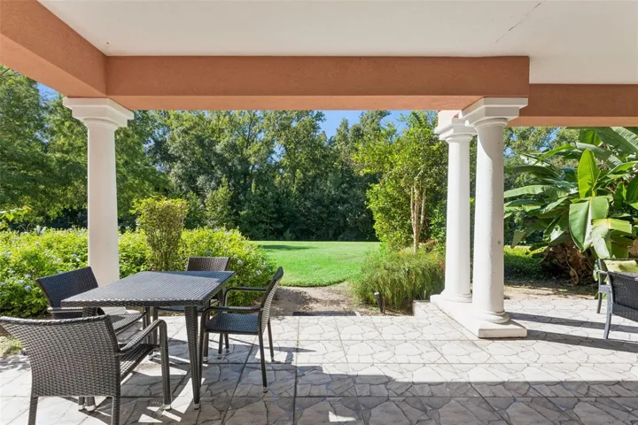 Covered Porch Lawn View: Direct view from the covered patio framed by architectural columns looking out onto an expansive green lawn and dense private tree line.