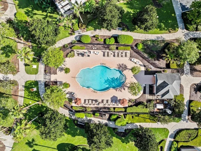 Overhead View of Community Pool: Direct top-down aerial view of the sparkling community pool, paved sun deck with loungers, pool house, and manicured landscaping.