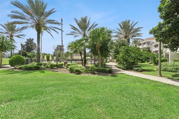Landscaped Grounds &amp; Courtyard: Ground-level view featuring manicured green lawns, paved walking paths, tropical palm trees, and gated access to the community pool facilities.