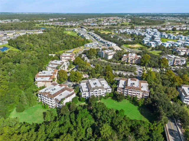 Community Layout Aerial: Broad aerial perspective showcasing the residential complex layout, expansive green spaces behind the buildings, and peaceful wooded surroundings.