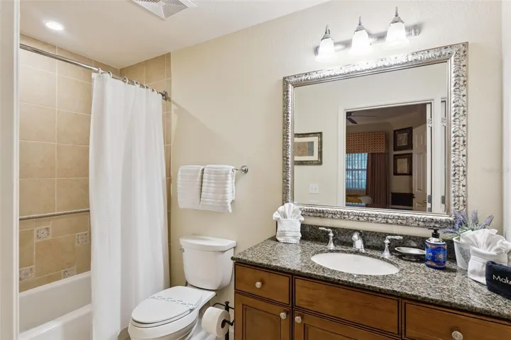 Additional Guest Bath: Well-maintained full bathroom offering a granite-topped vanity, framed mirror, multi-bulb lighting, and tub/shower enclosure.