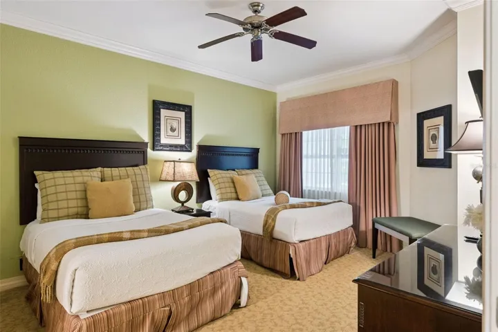 Double Guest Suite: Spacious guest bedroom offering two full beds, a soft green feature wall, central nightstand, ceiling fan, and a large draped window.