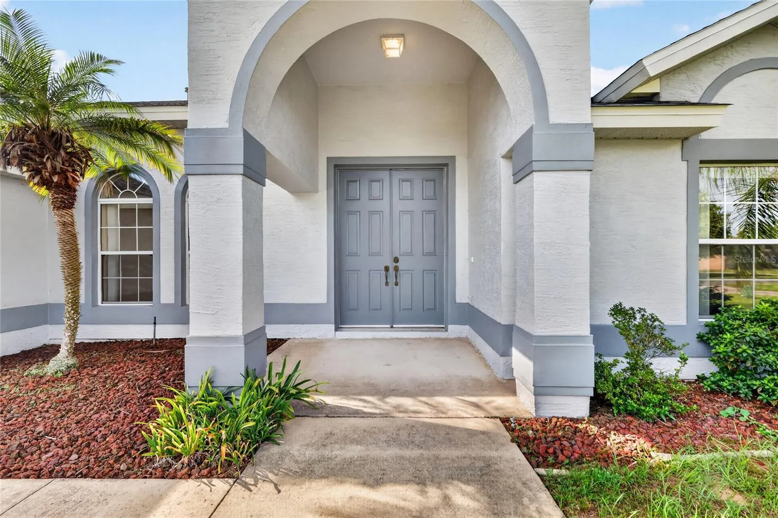 The covered front entry features an arched design, double doors, and landscaped surroundings.