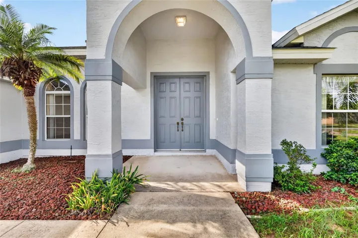 The covered front entry features an arched design, double doors, and landscaped surroundings.