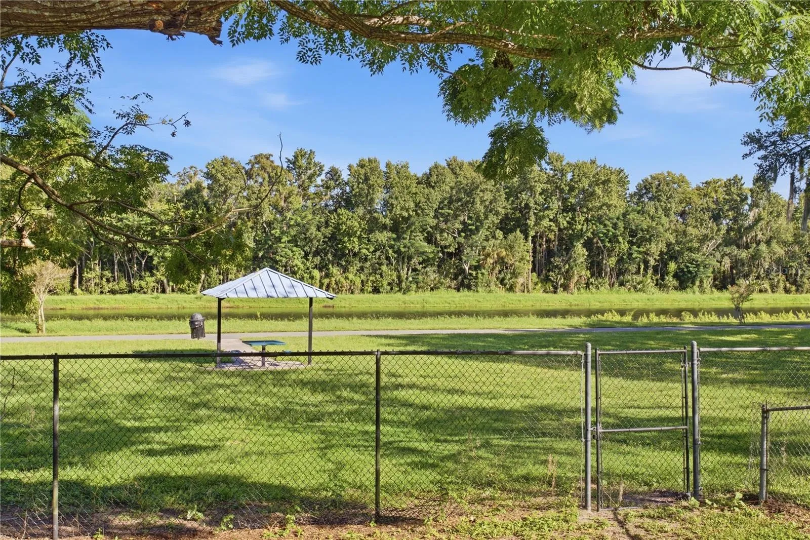 Fenced backyard with gate leading to trail, picnic table and river