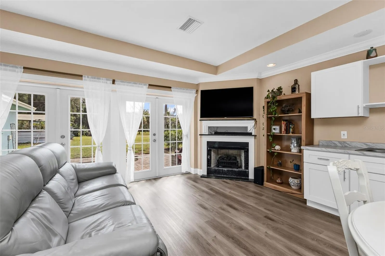 Open living room and kitchen with fireplace with French doors leading to paver patio