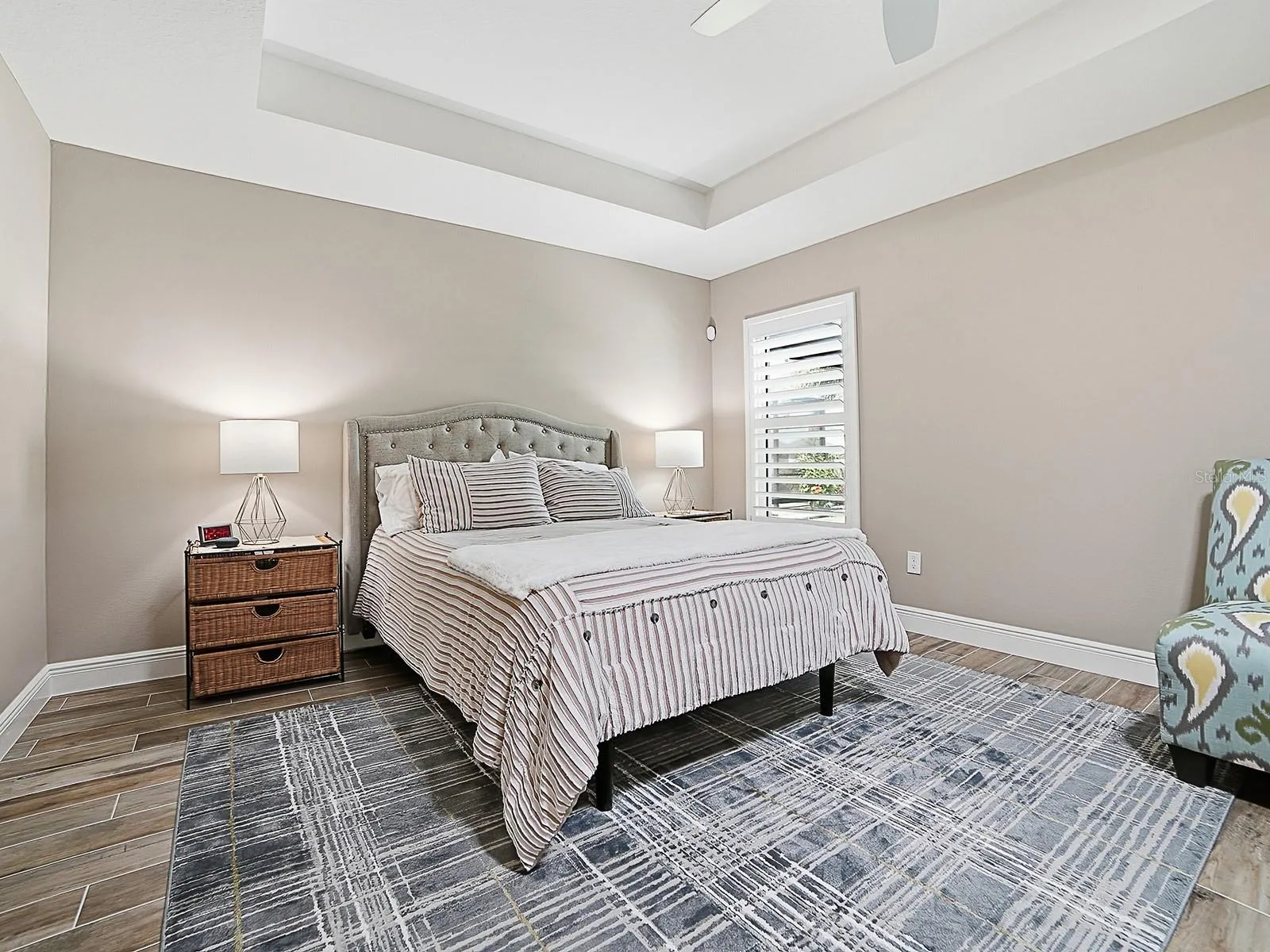PRIMARY BEDROOM WITH TRAY CEILING AND PLANTATION SHUTTERS.