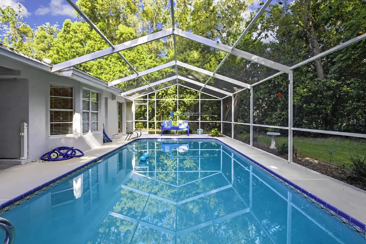 Screen-enclosed swimming pool surrounded by a private wooded setting